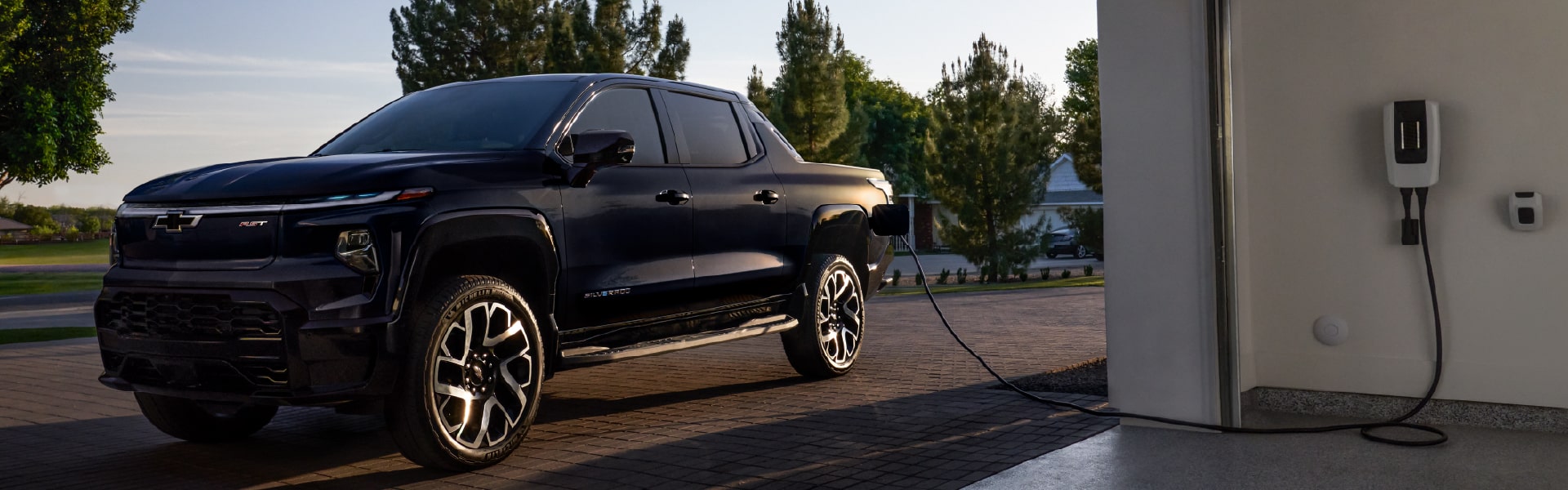 Electric truck charging in a driveway with trees in the background, featuring modern design elements.