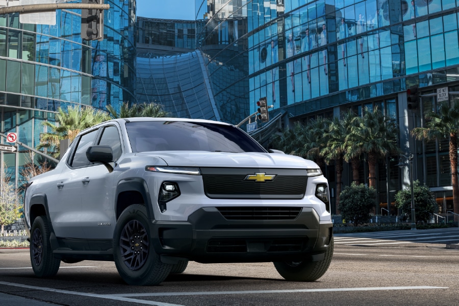 White Chevrolet pickup truck parked on urban street with glass buildings and palm trees.
