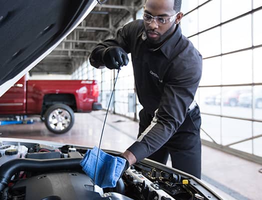 Mechanic checking engine oil with dipstick in a garage, focusing on vehicle maintenance.