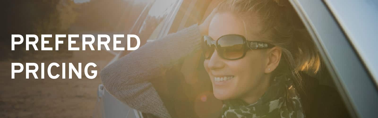 Smiling woman in sunglasses leaning out car window, "Preferred Pricing" text overlay.