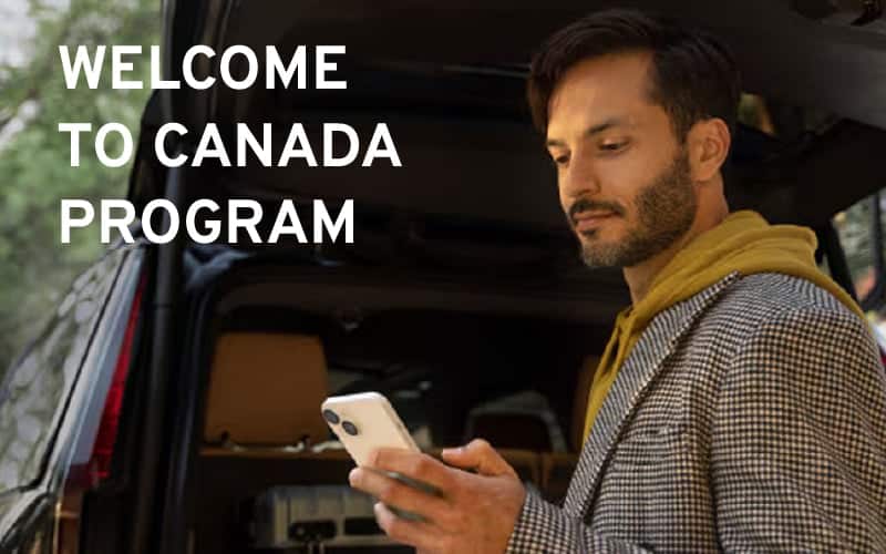 Man checking phone near car with "Welcome to Canada Program" text.
