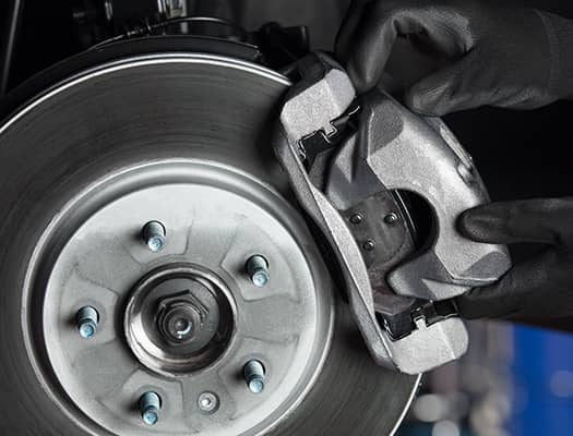 Mechanic wearing gloves installs a brake caliper on a car's brake rotor.
