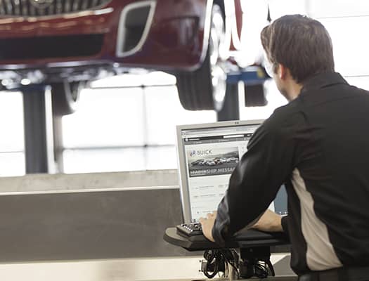 Mechanic using a computer next to a lifted car in an auto repair shop.